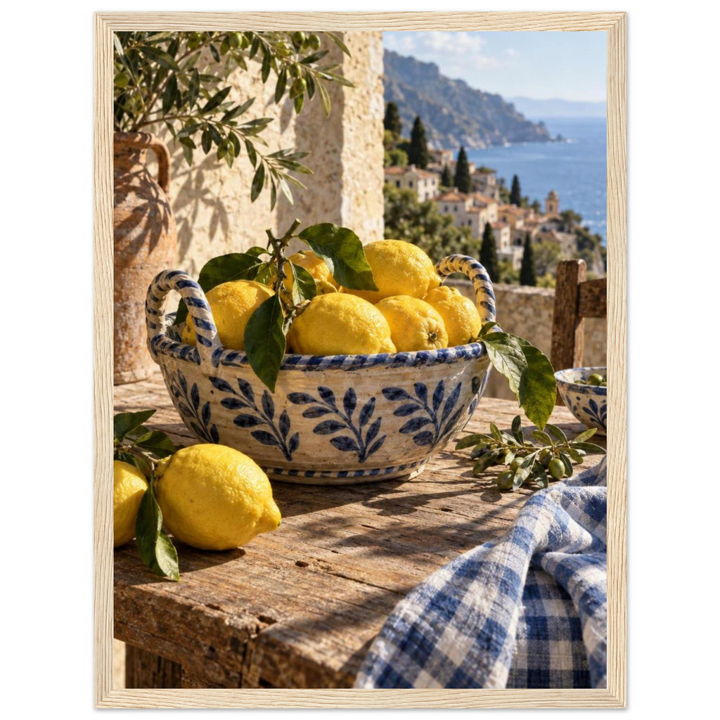 Lemons in a blue-and-white bowl on a wooden table, with olive branches, checked cloth and a coastal village beyond.