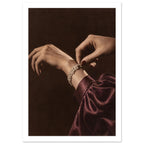 Hands adjusting a sparkling bracelet, with dark red nails and a gathered burgundy sleeve against a dark brown background.