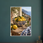 Lemons in a blue-and-white bowl on a wooden table, with olive branches, checked cloth and a coastal village beyond.
