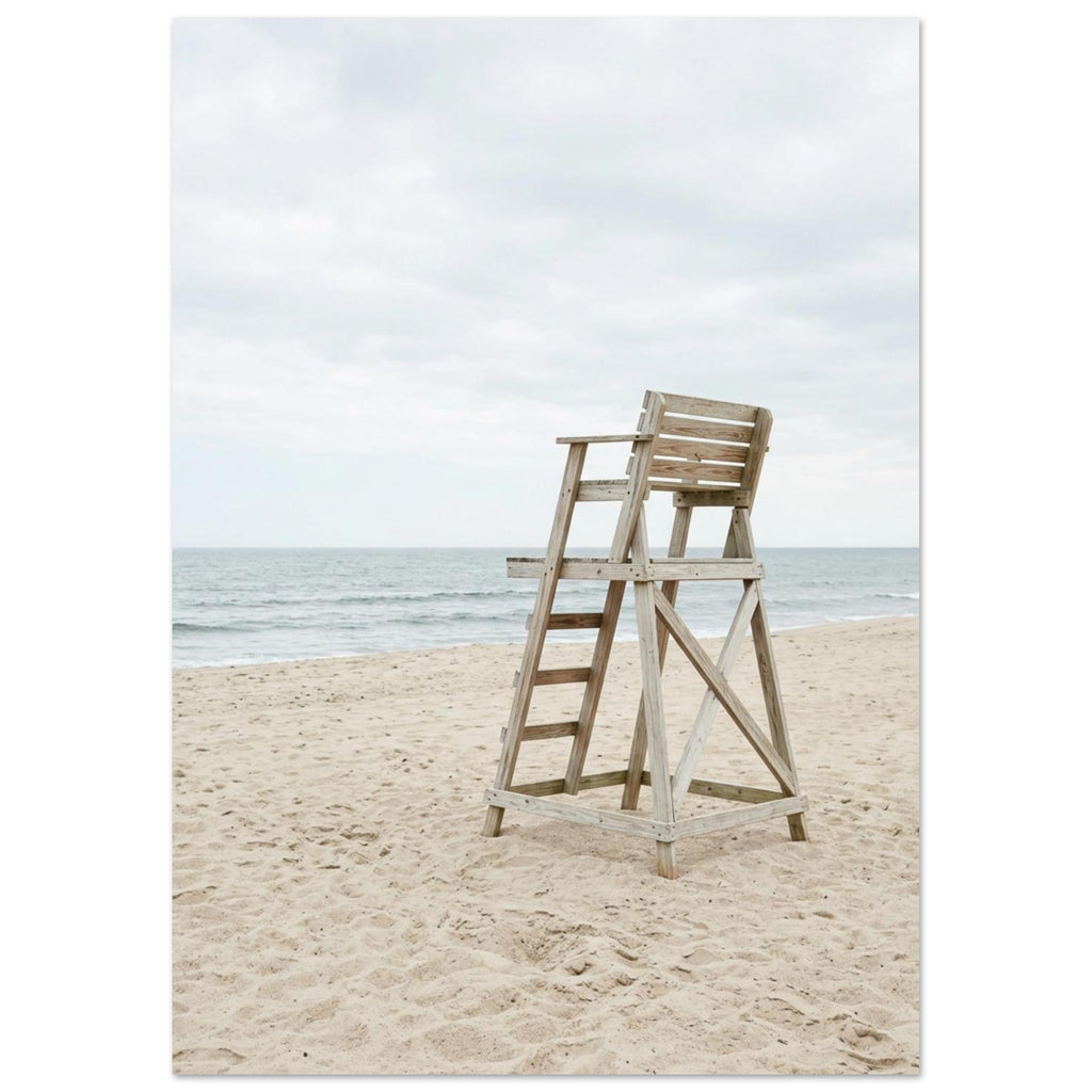 Empty wooden lifeguard chair on pale sand beside gentle sea waves beneath an overcast sky.