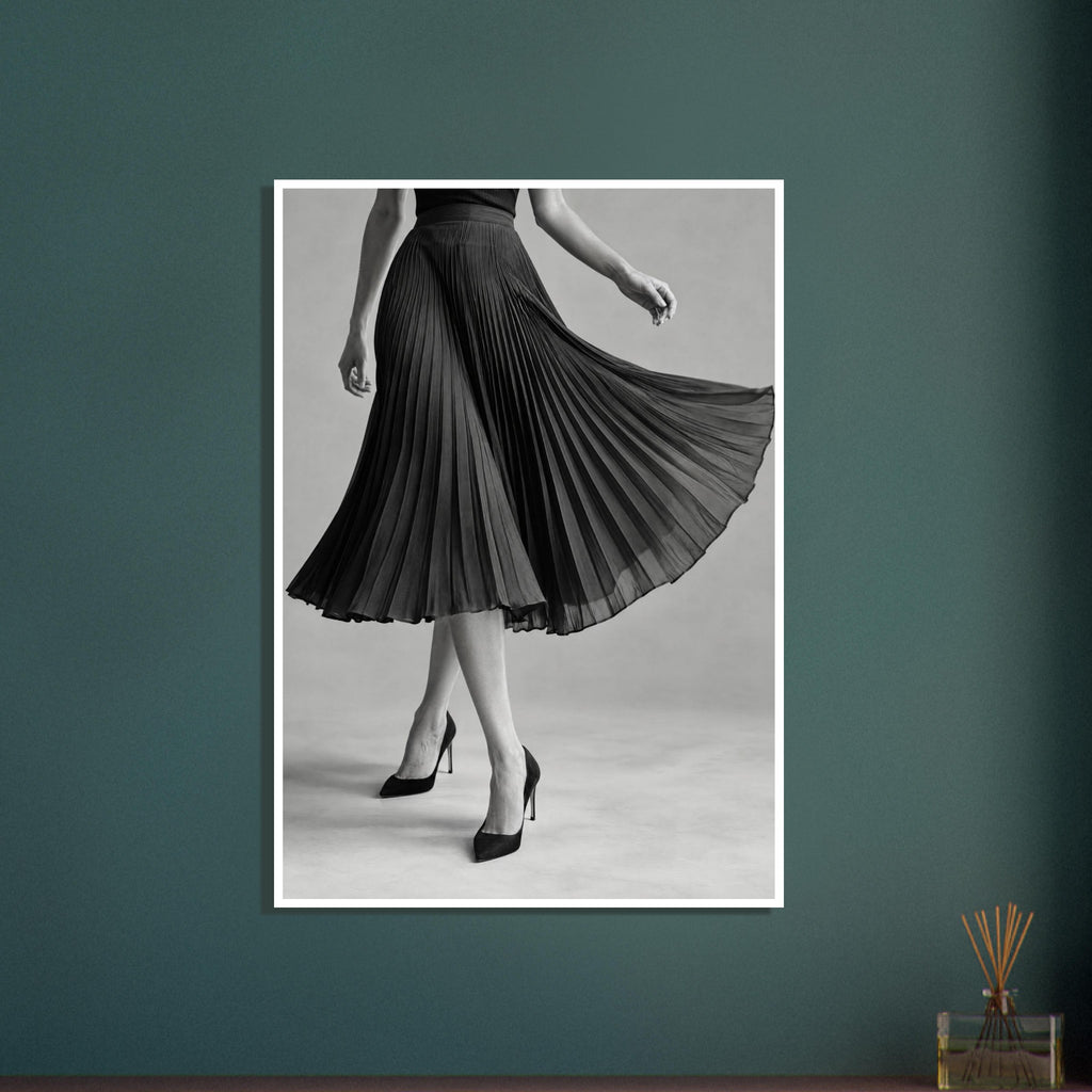 Cropped figure in a flowing black pleated skirt and pointed high heels, with crossed legs against a grey background.