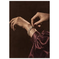 Hands adjusting a sparkling bracelet, with dark red nails and a gathered burgundy sleeve against a dark brown background.