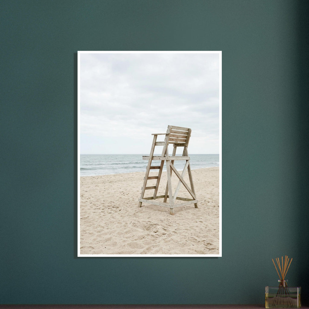 Empty wooden lifeguard chair on pale sand beside gentle sea waves beneath an overcast sky.