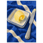 The Butter Curl still life showing a curled pat of butter on a rectangular dish beside a silver knife on cobalt cloth.