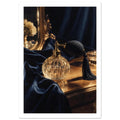 Faceted glass perfume bottle with black bulb and tassel on a golden tabletop beside navy drapery and an ornate mirror.