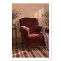 Burgundy armchair with an open book and lilac throw beside a table with flowers, books and a cup in a sunlit room.