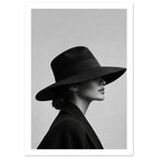 Woman in profile wearing a wide-brimmed black hat that covers her eyes and a dark coat against a plain grey background.