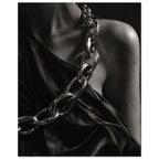 Oversized polished chain links cross dark, lustrous fabric beside a bare shoulder and neckline in black and white.
