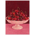Red and burgundy cherries in a pale pink pedestal bowl on a pink tabletop against a deep red painted background.