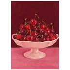 Red and burgundy cherries in a pale pink pedestal bowl on a pink tabletop against a deep red painted background.