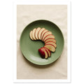 Red-skinned apple slices arranged in a curve on a green plate, photographed from above on cream fabric.