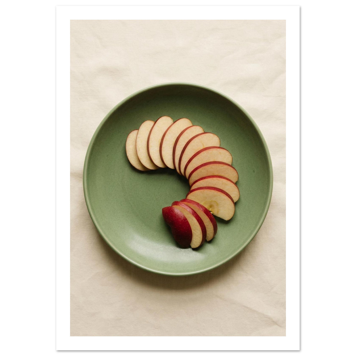 Red-skinned apple slices arranged in a curve on a green plate, photographed from above on cream fabric.