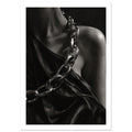 Oversized polished chain links cross dark, lustrous fabric beside a bare shoulder and neckline in black and white.