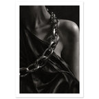 Oversized polished chain links cross dark, lustrous fabric beside a bare shoulder and neckline in black and white.