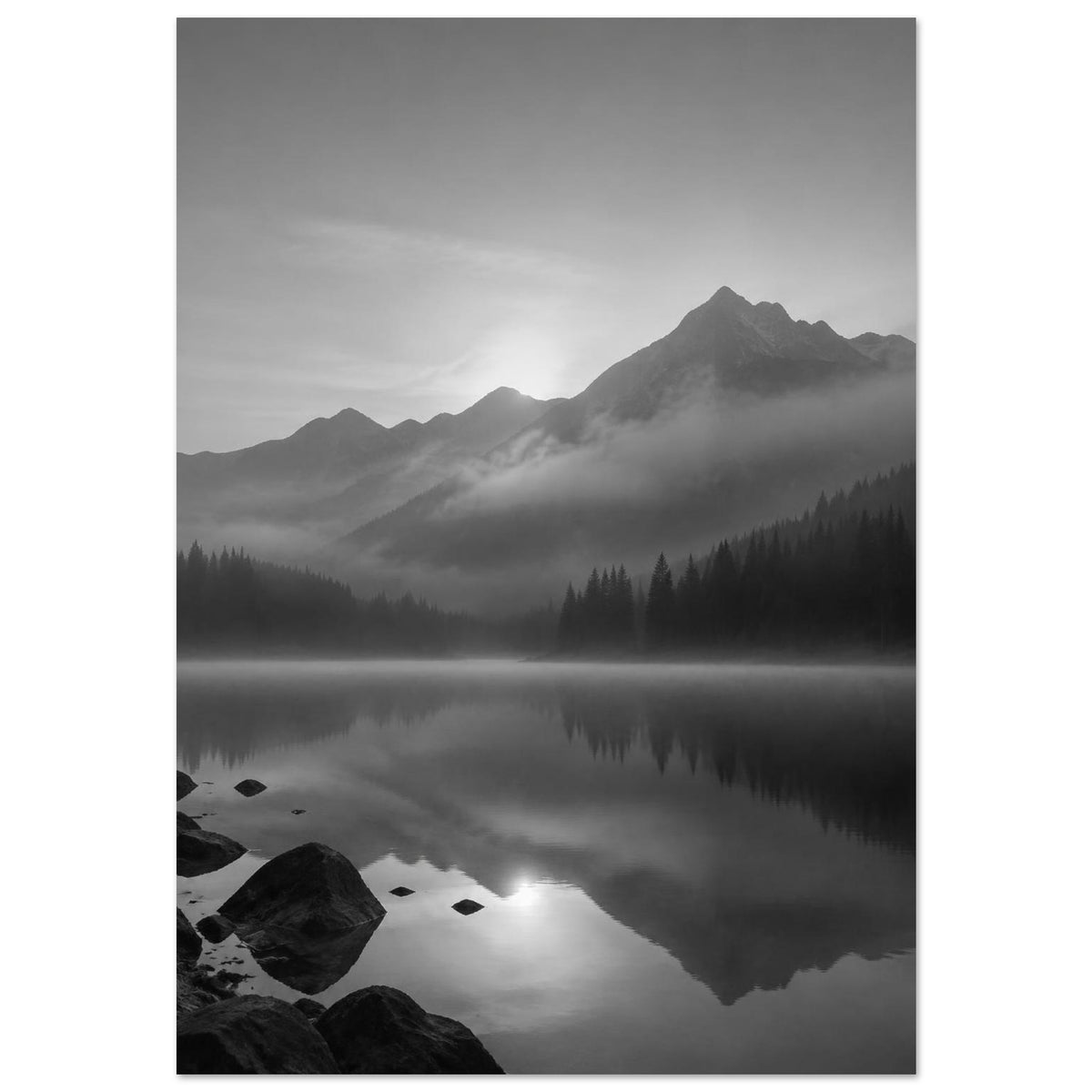 Mountain peaks and conifer forests reflected in a misty lake, with rocks in the foreground, in black and white.