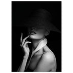 Woman in a wide-brim black hat hiding her eyes, with a hand near her chin and a white collar, in black and white.