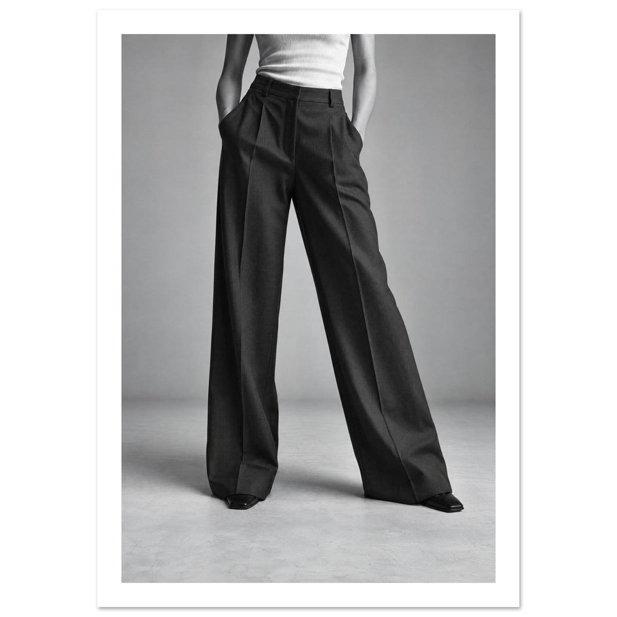 Cropped figure in dark wide-leg trousers, a white ribbed top and pointed shoes, standing with hands in pockets.