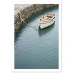 Cream wooden rowboat with oars, tied to a stone harbour wall above gently rippling blue-green water.