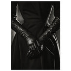 Overlapping hands in long black leather gloves against a dark fitted outfit, photographed in black and white.