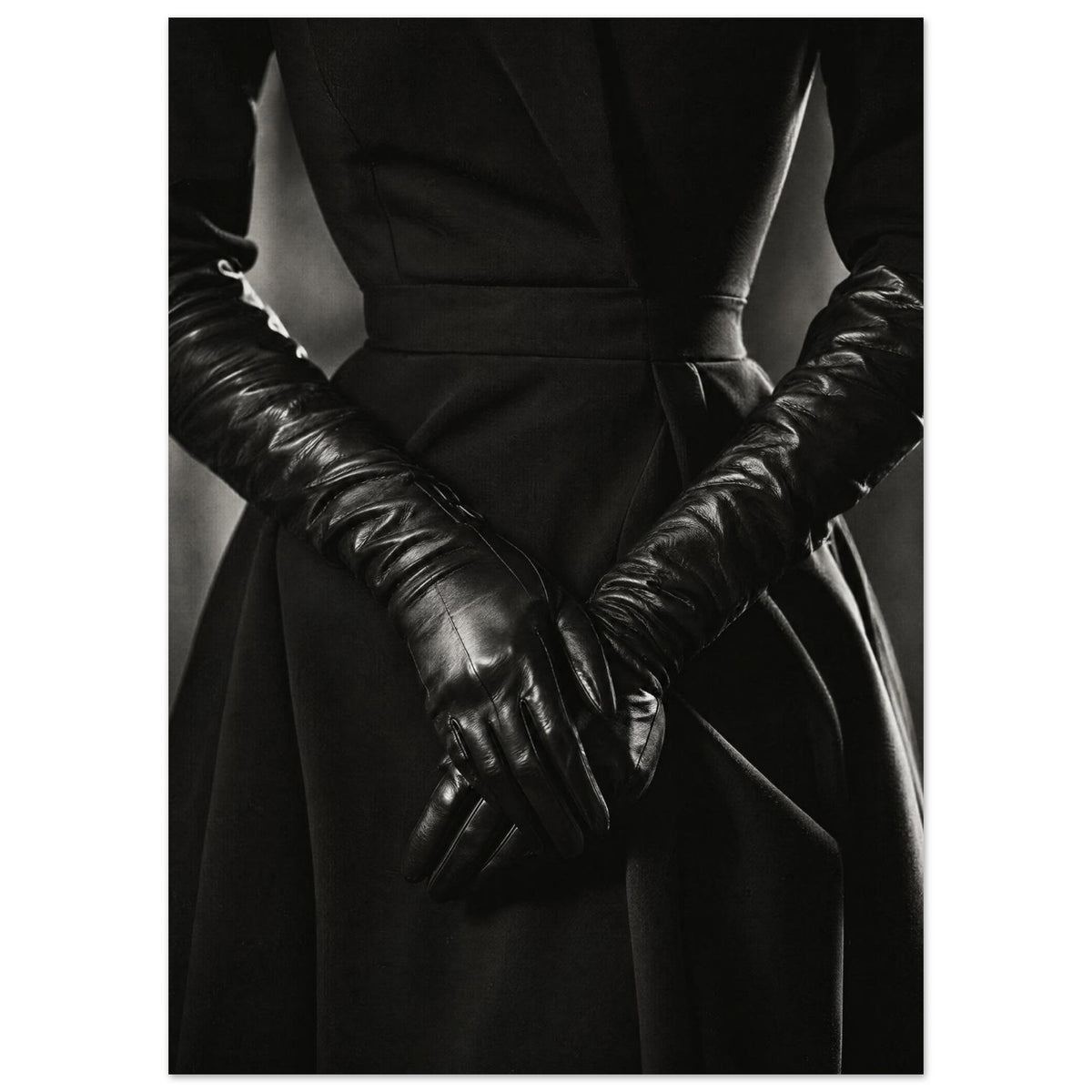 Overlapping hands in long black leather gloves against a dark fitted outfit, photographed in black and white.