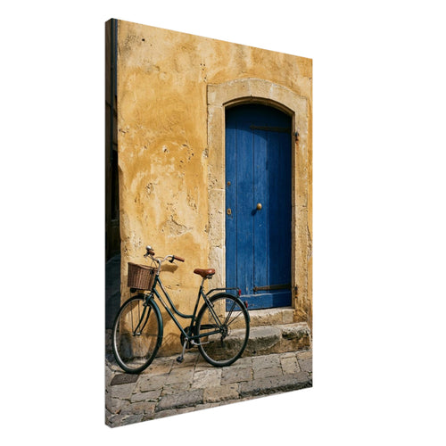 Green bicycle with a woven basket beside a blue wooden door in a golden plaster wall, above worn stone paving.