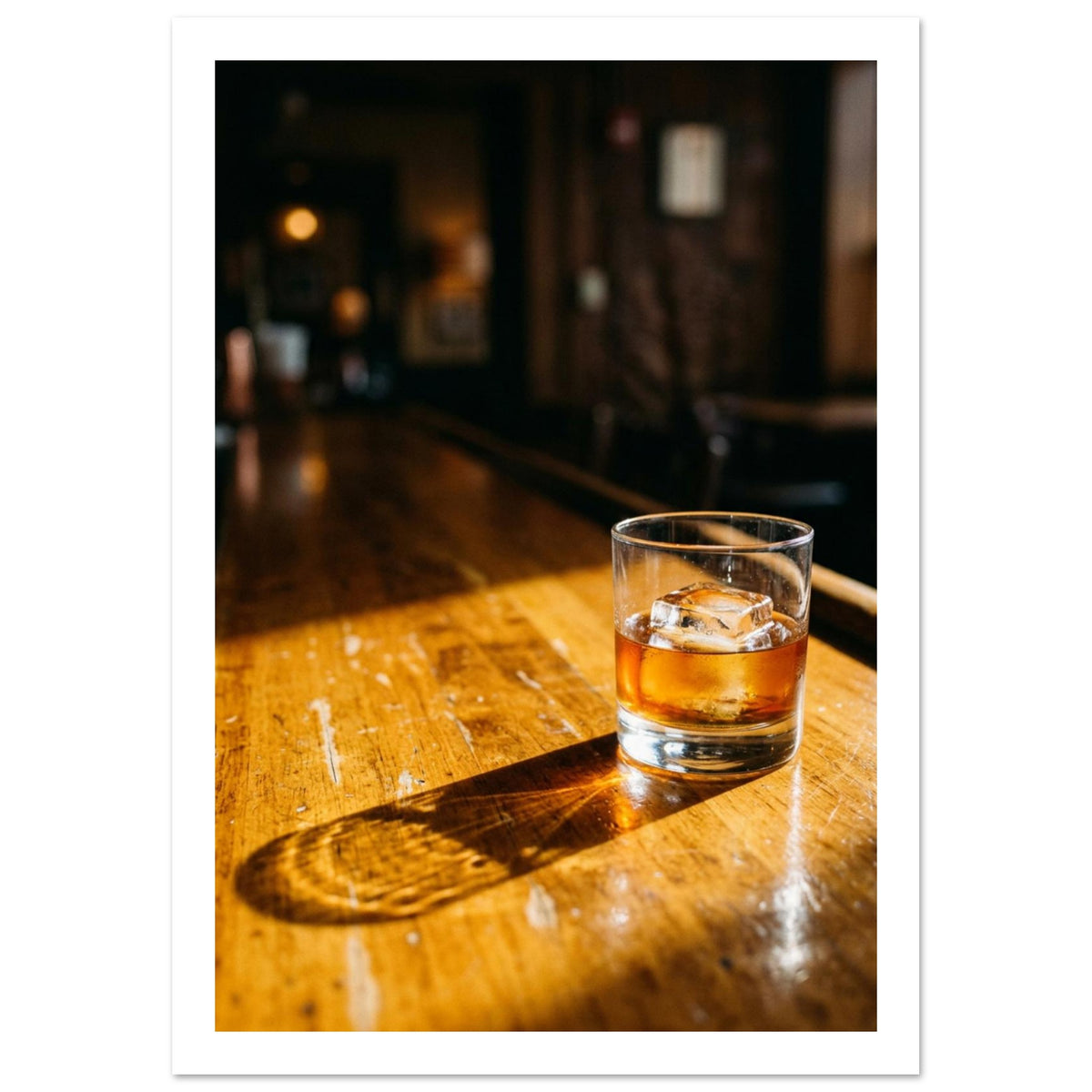 Tumbler of amber drink with ice on a sunlit wooden bar, casting a long shadow against a dark, blurred interior.