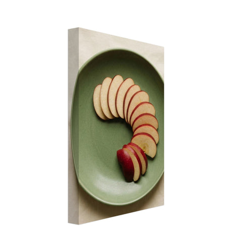 Red-skinned apple slices arranged in a curve on a green plate, photographed from above on cream fabric.