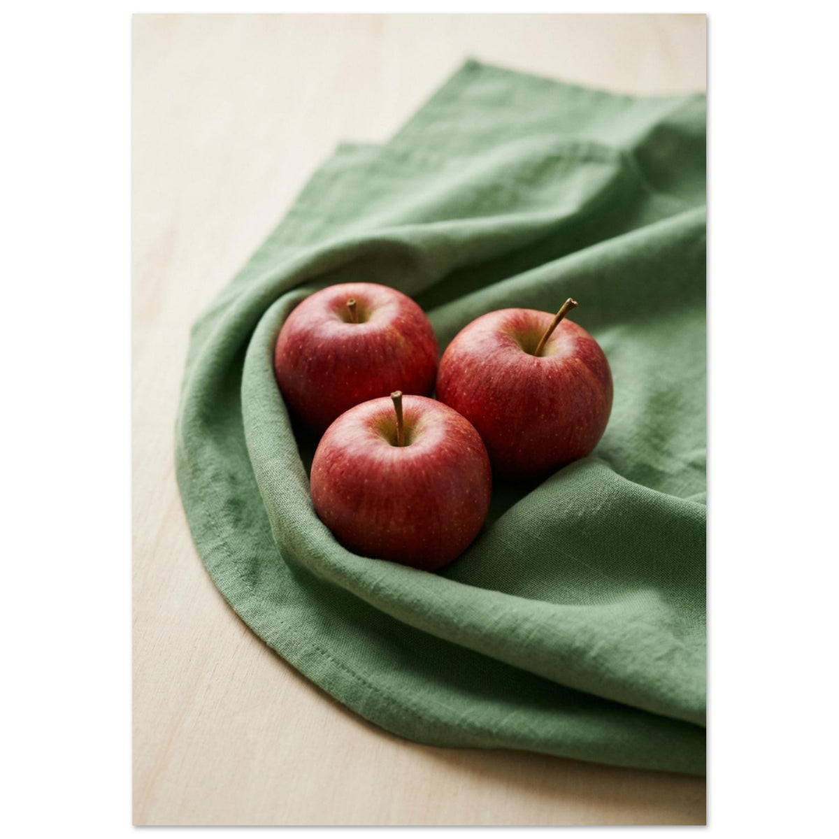 Red apples piled in a shallow green bowl on a cream surface, with soft shadows and a plain cream background.