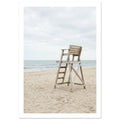 Empty wooden lifeguard chair on pale sand beside gentle sea waves beneath an overcast sky.