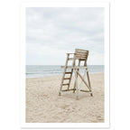 Empty wooden lifeguard chair on pale sand beside gentle sea waves beneath an overcast sky.
