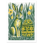 Green and yellow hare beside a floral-patterned Easter egg, surrounded by tall grass and yellow flowers on off-white.
