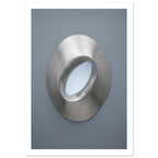 Brushed silver oval ring with a tilted opening, soft highlights and shadows against a blue-grey background.