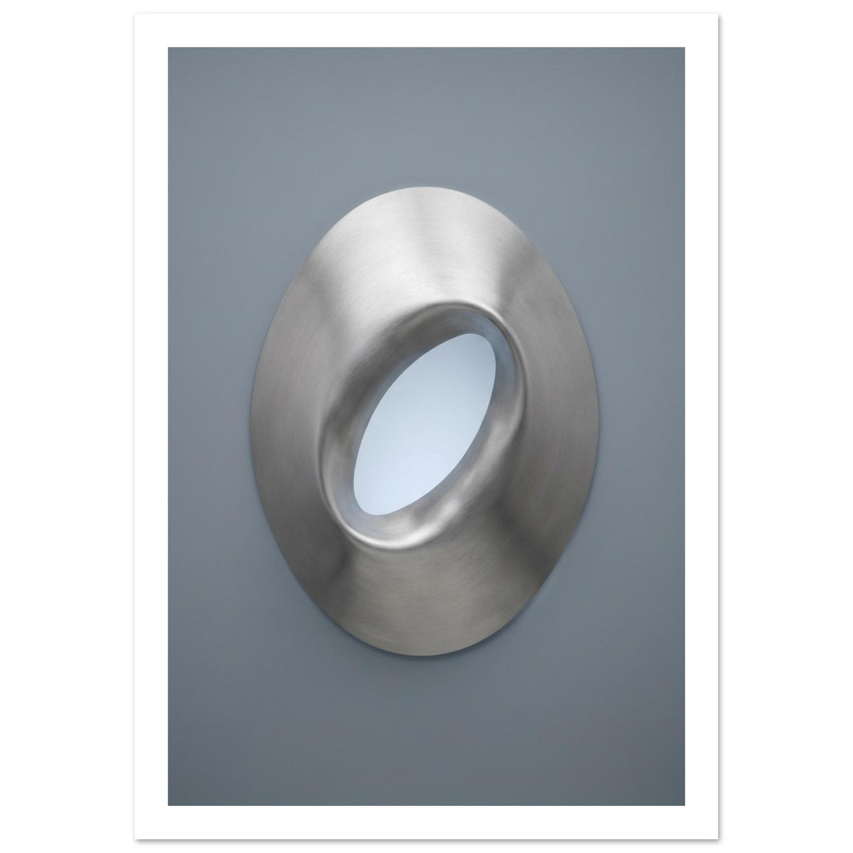 Brushed silver oval ring with a tilted opening, soft highlights and shadows against a blue-grey background.