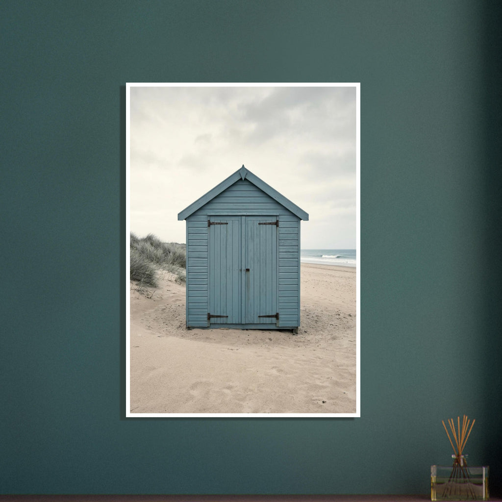 Blue wooden beach hut with closed doors on pale sand, with dune grasses, sea waves and an overcast sky.