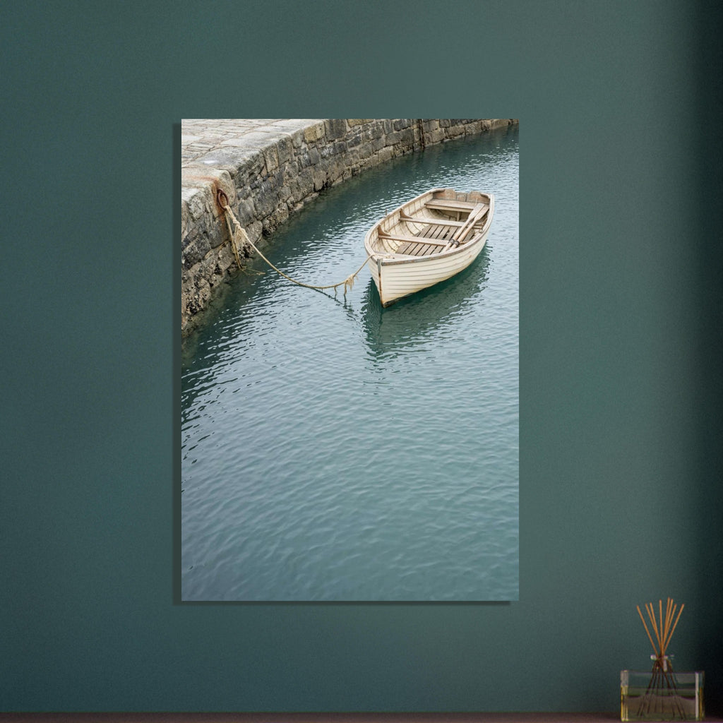 Cream wooden rowboat with oars, tied to a stone harbour wall above gently rippling blue-green water.
