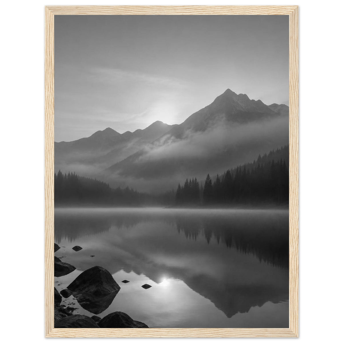 Mountain peaks and conifer forests reflected in a misty lake, with rocks in the foreground, in black and white.