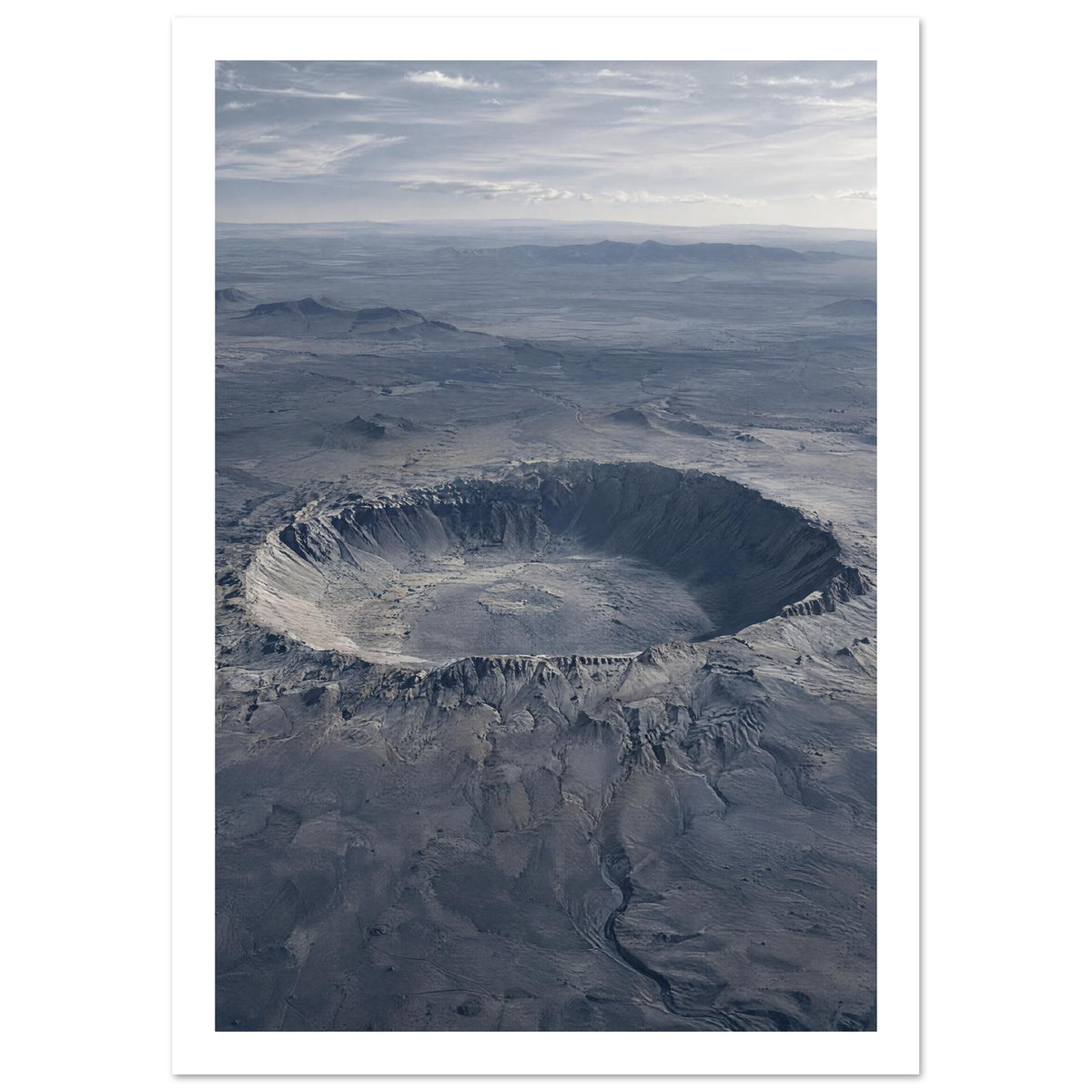Large circular crater in a blue-grey desert plain, with rugged slopes, distant hills and a cloudy sky.
