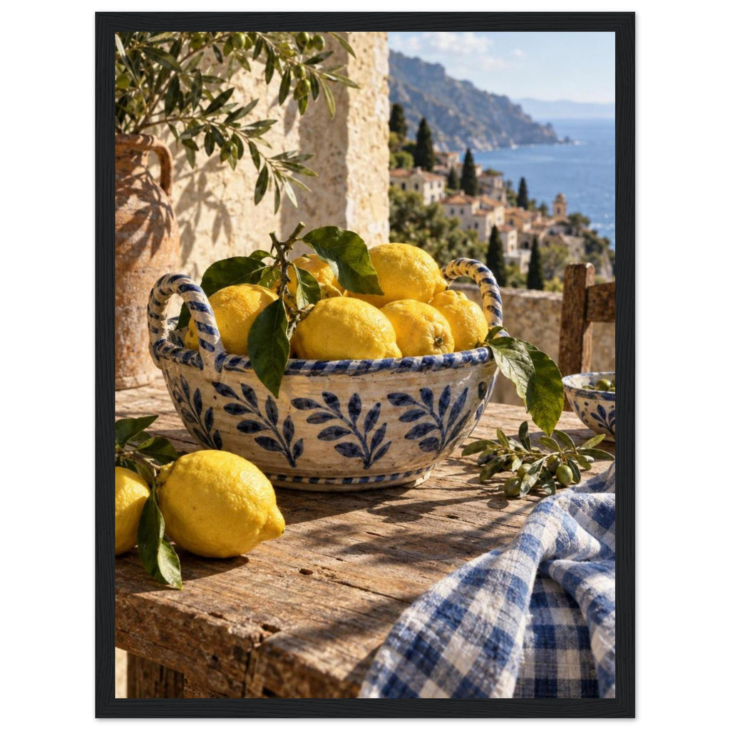 Lemons in a blue-and-white bowl on a wooden table, with olive branches, checked cloth and a coastal village beyond.