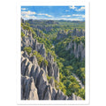 Jagged grey stone pinnacles rising through dense green forest beneath a blue sky with scattered white clouds.