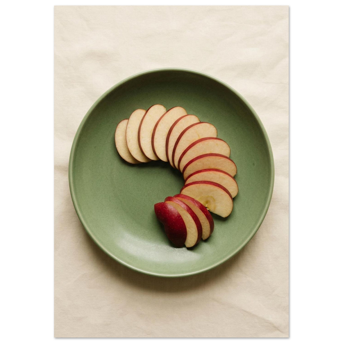 Red-skinned apple slices arranged in a curve on a green plate, photographed from above on cream fabric.