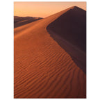 Desert sand dune with rippled orange slopes, a sweeping ridge and deep brown shadow beneath a peach sky.