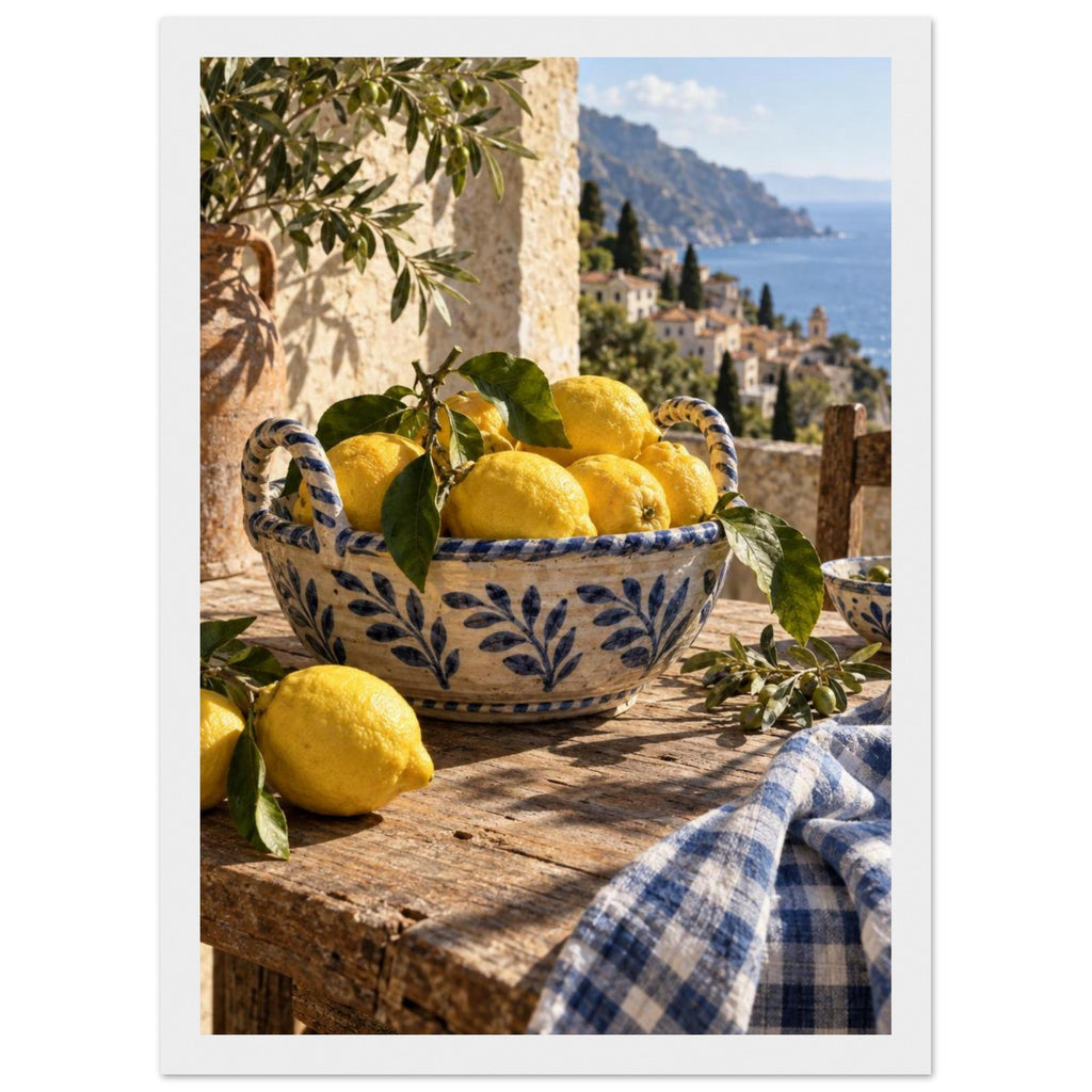Lemons in a blue-and-white bowl on a wooden table, with olive branches, checked cloth and a coastal village beyond.