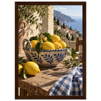Lemons in a blue-and-white bowl on a wooden table, with olive branches, checked cloth and a coastal village beyond.
