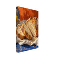 Sliced crusty loaf on cream cloth over a blue table, with lemons, pottery and olive branches against an orange backdrop.