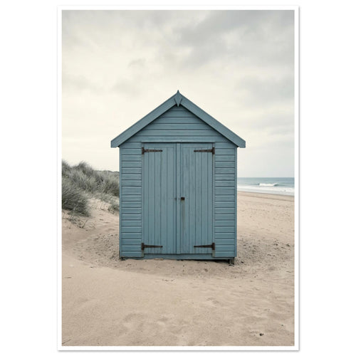 Blue wooden beach hut with closed doors on pale sand, with dune grasses, sea waves and an overcast sky.