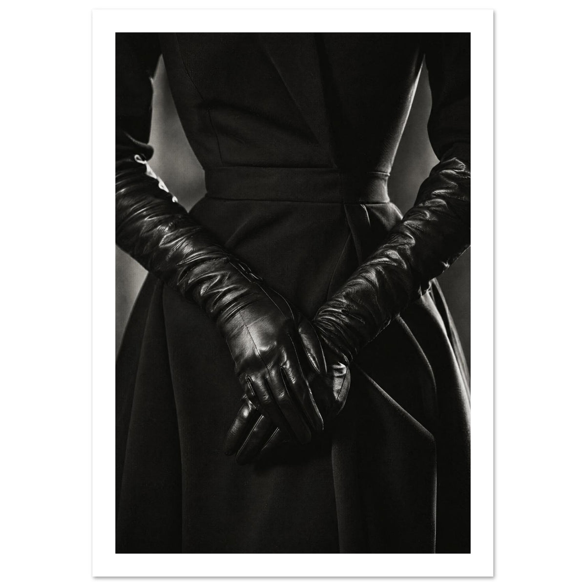 Overlapping hands in long black leather gloves against a dark fitted outfit, photographed in black and white.