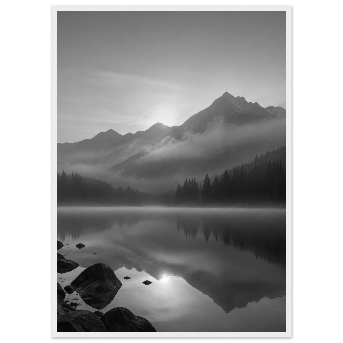 Mountain peaks and conifer forests reflected in a misty lake, with rocks in the foreground, in black and white.