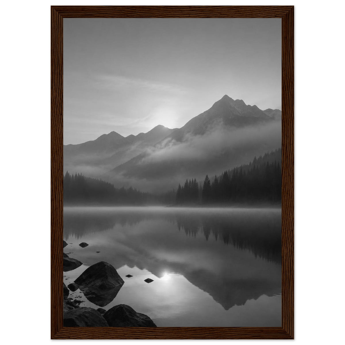 Mountain peaks and conifer forests reflected in a misty lake, with rocks in the foreground, in black and white.