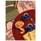 Two blue coffee cups, a peeled orange, spoon and yellow cloth on a red table beside a green woven chair and pink tiles.