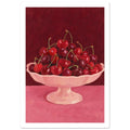 Red and burgundy cherries in a pale pink pedestal bowl on a pink tabletop against a deep red painted background.